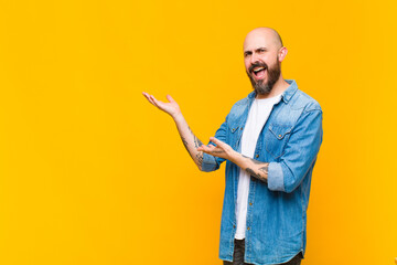 young bald and bearded man smiling proudly and confidently, feeling happy and satisfied and showing a concept on copy space