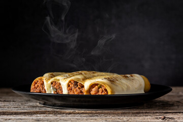 Wall Mural - Hot meat cannelloni pasta on rustic wooden table	 and black background