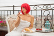 beautiful young female with red hair in a white towel eats strawberries at a table on the terrace