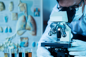 doctor or scientist wear medical face mask and looking in microscope while working on medical resear