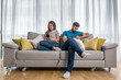 © Srdjan - Young couple sitting on the sofa in the living room and ignoring each other by surfing and text messaging on their smartphones, relationship difficulties and issues concept