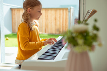 Portrait of pretty little girl having piano lesson at modern white e-piano