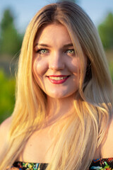 overlight bright portrait of a charming attractive blonde in flowery dress in the field. 