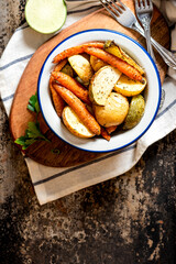 Sticker - Baked vegetables. Roasted potatoes, carrots and radish with herbs in a bowl on a dark background top view. Vegetarian food, rustic style. Copy space.