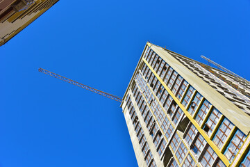 Facade of a new modern high-rise residential building. Skyscraper on blue sky background. Tall house renovation project, government programs. Minimalistic multi storied home. Urban architecture