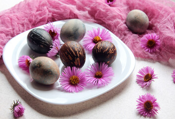 Wall Mural - Painted Easter eggs with lilac flowers on a white plate on the background of a delicate napkin, close - up