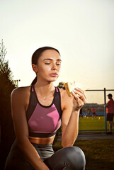 Woman eating a sandwich after a workout. Athlete resting on a background of sunset.