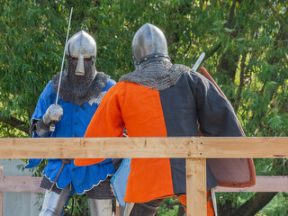 Two knights on foot in heavy medieval armor fight with swords. They are protected by iron helmets and shields. Historical reconstruction of medieval European knightly tournaments