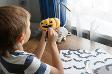 Close Up Image Of Boy Getting Ready For Halloween Party, Holding Pumpkin In His Hands And Drawing Black Face On It. Halloween Concept.