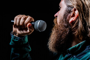 Wall Mural - Male singing with a microphones. Man with a beard holding a microphone and singing. Bearded man in karaoke sings a song into a microphone. Male attends karaoke