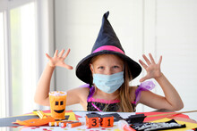 A Little Girl In A Witch Costume In A Medical Mask Makes Crafts And Scares.