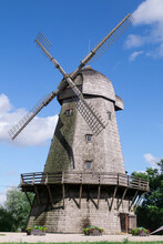 Summer Shot Of Historical Old Wooden Windmill With Blue Cloudy Sky Background. Authentic Unique Wooden Windmill With A Balcony Typical For 18th Century For Several European Countries Denmark, Holland
