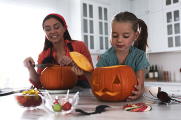 Poster - Mother and daughter making pumpkin jack o'lantern at table in kitchen. Halloween celebration