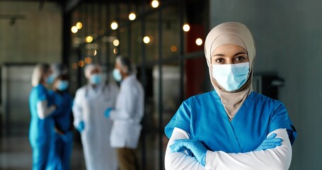 Portrait of Arab woman doctor in hijab, medical mask and gloves standing in hospital. Muslim female medic in traditional headscarf in clinic. Covid-19. Arabian nurse. Coronavirus. Protected.