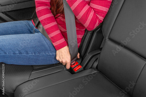 A woman fastening seat belt in back seat of car.