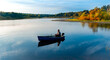 © Sergey + Marina - Elderly man fishing with a rod on a small fishing boat on the lake at autumn sunset