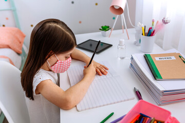 Wall Mural - Top view of girl with mask doing homework sitting at a desk in her bedroom