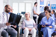 © DC Studio - Doctor with stethoscope holding disabled senior woman radiography in wheelchair while talking with her in hospital waiting area. Patient asking about his appointment at clinic reception.