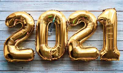 Number 2021 made from golden inflated balloons on a rustic wooden table along with coronavirus vaccine. Happy new year two thousand twenty-one wishing the end of pandemic