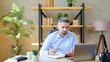 © viacheslav - Confused bearded business man sits on chair at table in home office wear wireless earphones works distance online remote video call chat conference with employees, uses laptop computer webcam