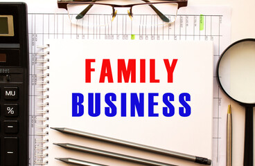 Office desk with financial papers, magnifying glass, calculator, glasses. Notepad page with the text FAMILY BUSINESS.