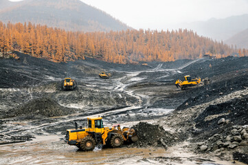 Wall Mural - Open pit mining (natural gold) in mountainous areas. A bulldozer collects a pile of mountain soil. Then, wheel loaders transport this mountain soil and dump it into industrial washing equipment in ord