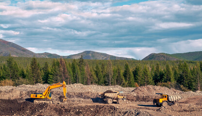 Wall Mural - Excavator loads mountain soil into the body of a mining dump truck and then transports the load. Extraction of minerals in the mountainous region of Eastern Siberia