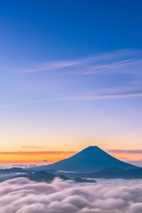 The peaks of Mount Fuji in summer rise above the clouds and the light of the sky during the sunrise