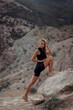 © strekozza77 - Sportive woman in trendy sports outfit trains in the street. Fitness model doing exercises in the park against the backdrop of mountains and ocean. Yoga. Sports Warm-up. Run.