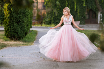 Blonde woman with make up in evening dress at park. The skirt of her dress fly on a wind. Sensual fashion portrait with a sunset light