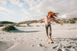 canvas print picture - Junge Frau tanz mit fliegenden kupferfarbenen Haaren am Strand von Amrum