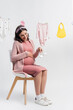 © LIGHTFIELD STUDIOS - pleased pregnant woman holding tiny boots and sitting near near baby clothes on white