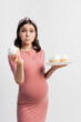 © LIGHTFIELD STUDIOS - pregnant woman holding plate while eating cupcake isolated on white