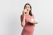© LIGHTFIELD STUDIOS - joyful pregnant woman holding plate while eating cupcake isolated on white