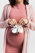 © LIGHTFIELD STUDIOS - cropped view of pregnant woman holding baby boots isolated on white