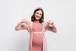 © LIGHTFIELD STUDIOS - joyful and pregnant woman pointing with fingers at belly on white