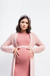 © LIGHTFIELD STUDIOS - worried pregnant woman in headband touching belly isolated on white