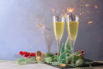 Two glasses with champagne and sparklers with Christmas trees miniatures,fir branches,beads and christmas decorations.Christmas card with copy space.