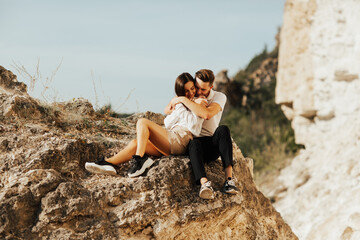 Wall Mural - Young couple are hugging and sitting on the stone on the mountain. Romantic tender couple are enjoying time together.