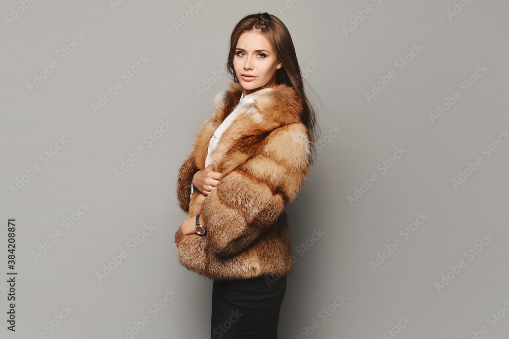 Side view of a model girl in a luxurious fur coat at the grey background. Winter fashion - obrazy, fototapety, plakaty 