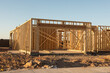 A partial view of a new house construction showing the wood frame before the siding and roofing stands in early morning light on a dirt lot, horizontal view.