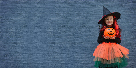 Wall Mural - Halloween trick or treat. Portrait smiling girl in witch hat against a blue wall . Copy space for text