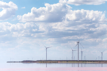 Wind generators farm on pink salt lake coast. Epic cloudy bright blue sky cloudscape with pink coloration