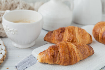 Delicious breakfast with fresh croissants and cup of coffee on a white wooden background. Delicious Baking