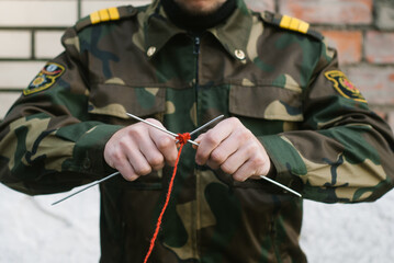 a soldier in uniform knits with needles and red thread,