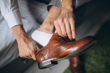 Wall Mural - Groom is wearing shoes indoors. Male portrait of handsome guy. Beautiful model boy in colorful wedding clothes. Man is posing