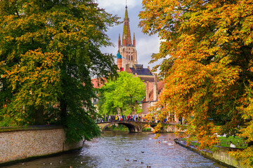 Bruges, Flanders, Belgium, Europe - October 1, 2019. Channels with white swans in the autumn of Bruges (Brugge) with the church of Our Lady in the background