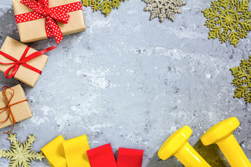 Wall Mural - Exercise, fitness and developing the concept of a merry Christmas and a happy New year. Yellow dumbbells, fitness bands and gifts on a concrete background. Top view, copy space