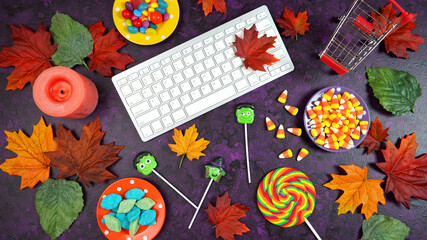 Wall Mural - Happy Halloween Trick or Treat theme desktop with candy and lollipops, autumn leaves on stylish purple textured background. Top view blog hero header creative composition flat lay.