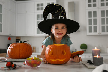 Canvas Print - Little girl with pumpkin jack o'lantern at table in kitchen. Halloween celebration